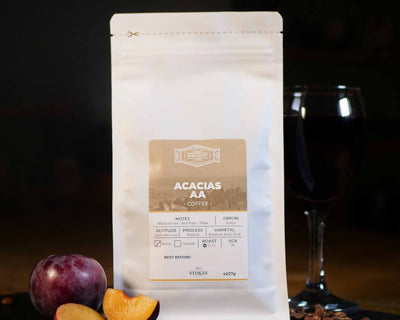 Acacias AA Coffee Beans in a white bag with a glass of red wine and a plum to show off the tasting notes