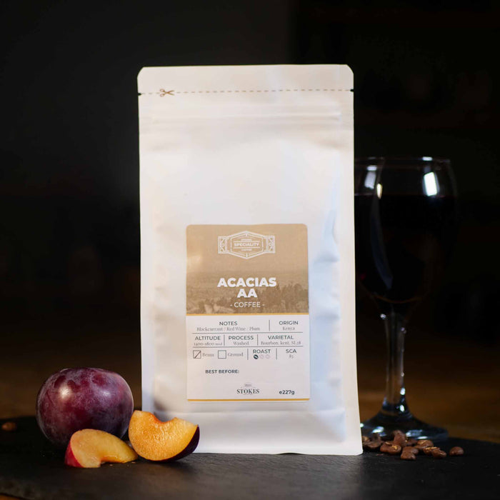 Acacias AA Coffee Beans in a white bag with a glass of red wine and a plum to show off the tasting notes