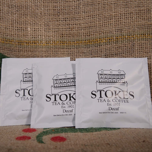 3 white coffee bags branded with Stokes on top of a hessian coffee sack