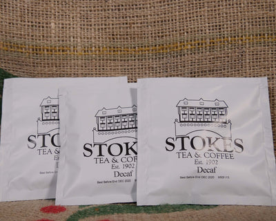 3 white coffee bags branded with Stokes on top of a hessian coffee sack