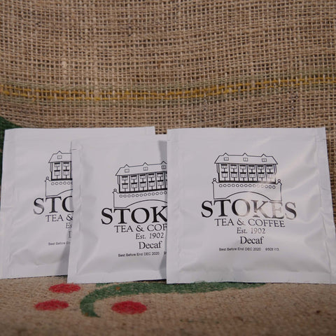 3 white coffee bags branded with Stokes on top of a hessian coffee sack